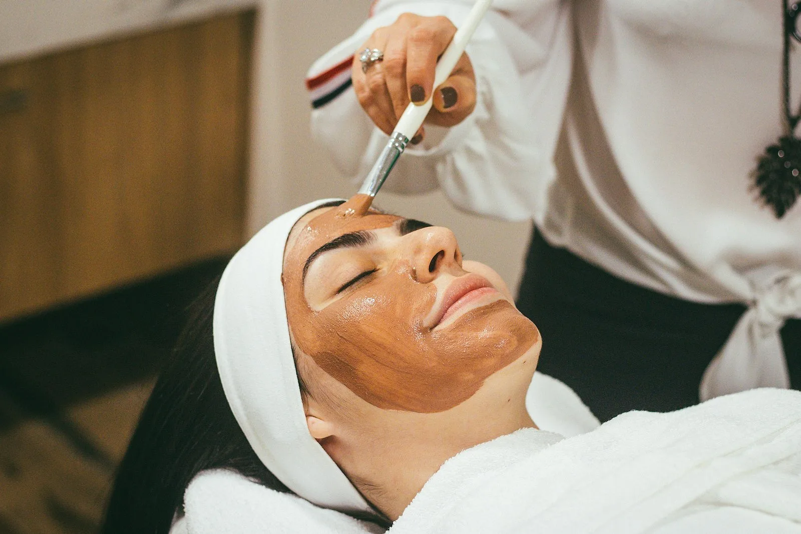 Una mujer recibe un cuidado facial con pincel, con los ojos cerrados